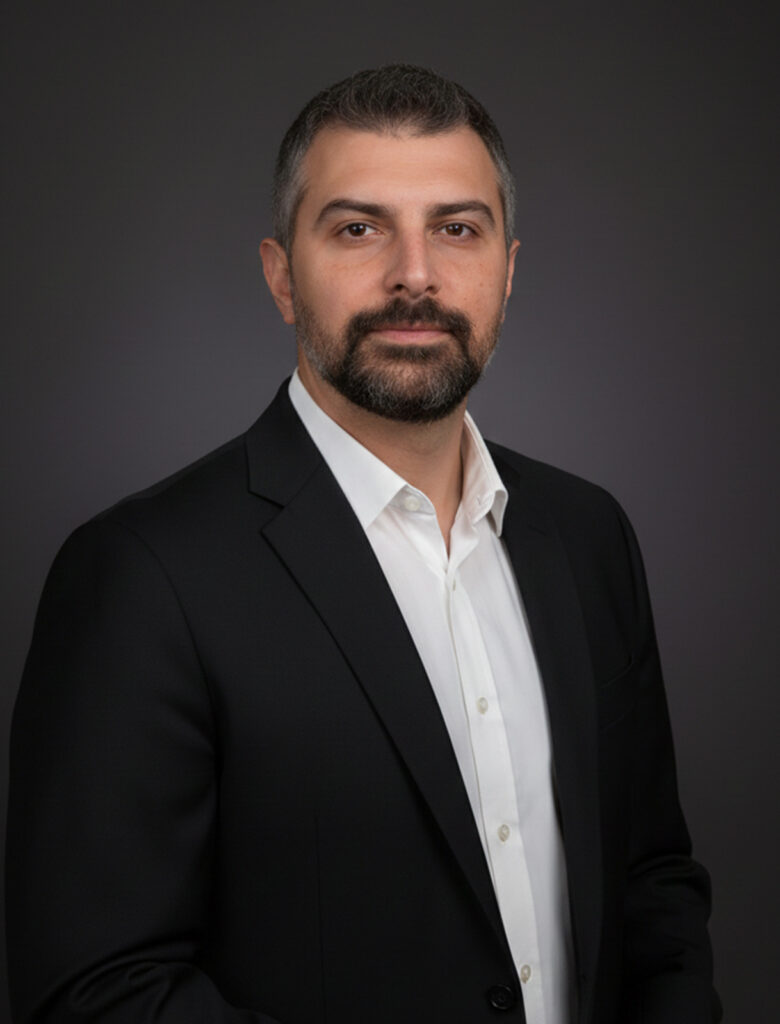 Portrait of Andrija Gramatikovski in a dark blazer and white shirt, standing against a neutral background, looking directly at the camera.